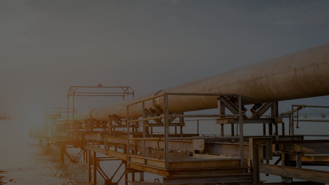 A large oil pipeline running along an offshore jetty at sunset