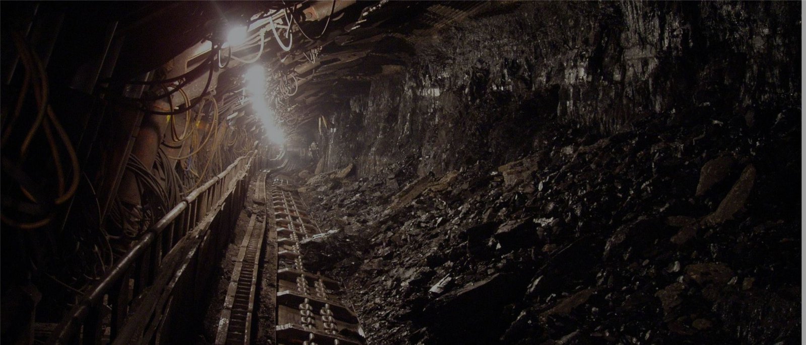 An underground mine tunnel with a conveyor, cables and bright lamps