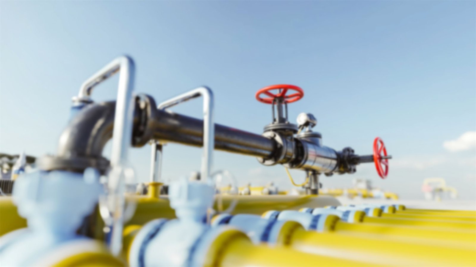 Gas pipeline with yellow pipes and red valve wheels under a blue sky